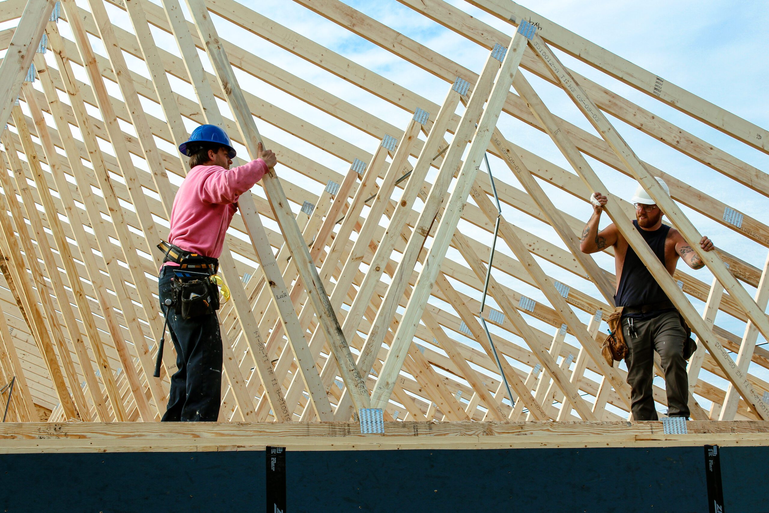 Two construction workers installing roof trusses on a new building during framing stage