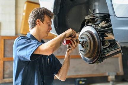 Auto Mechanic Servicing Brake Rotors on Lifted Car – Professional Vehicle Maintenance - Ink & Arrow Marketing Co. Mechanic working on car rotors while vehicle is lifted in a professional auto repair shop